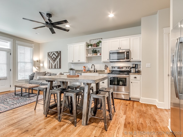 kitchen with light wood-type flooring, backsplash, a kitchen breakfast bar, white cabinetry, and stainless steel appliances