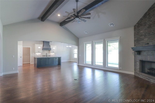 unfurnished living room featuring dark hardwood / wood-style floors, ceiling fan with notable chandelier, a fireplace, sink, and beam ceiling