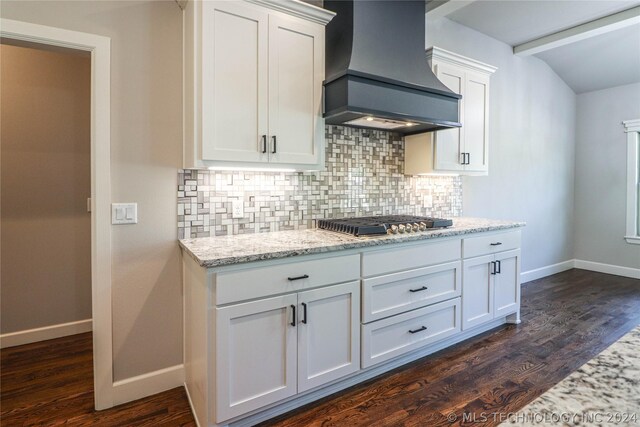 kitchen with dark wood-type flooring, white cabinetry, light stone counters, custom range hood, and decorative backsplash