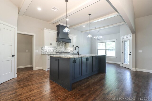 kitchen with premium range hood, sink, white cabinetry, light stone counters, and pendant lighting