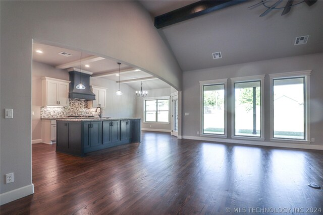 kitchen with white cabinetry, decorative backsplash, custom exhaust hood, hanging light fixtures, and a kitchen island with sink