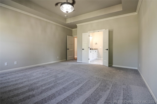 unfurnished bedroom with crown molding, light colored carpet, ensuite bathroom, and a tray ceiling