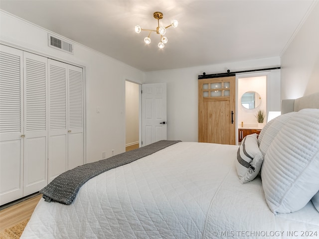 bedroom with a barn door, crown molding, a closet, a notable chandelier, and light wood-type flooring