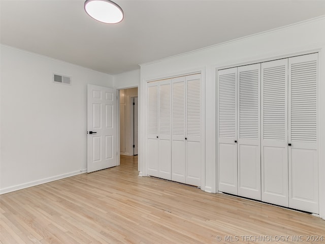 unfurnished bedroom with ornamental molding, light wood-type flooring, and multiple closets