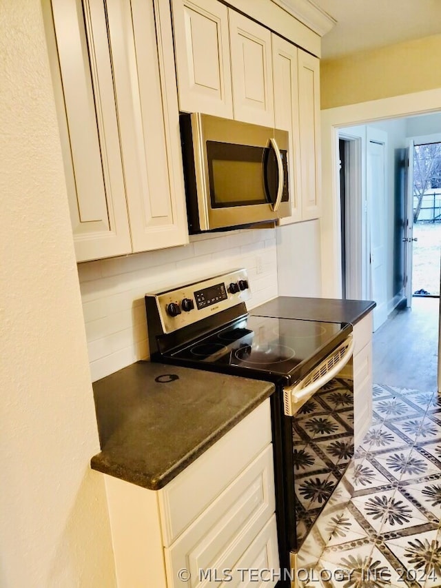 kitchen with appliances with stainless steel finishes, white cabinets, backsplash, and light tile floors