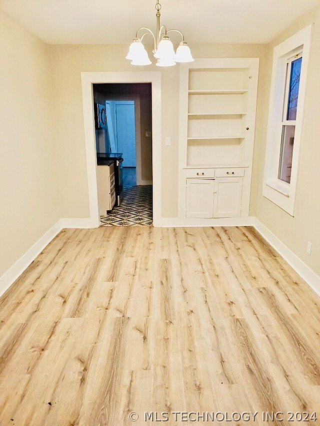 unfurnished dining area with a notable chandelier, light wood-type flooring, and built in shelves