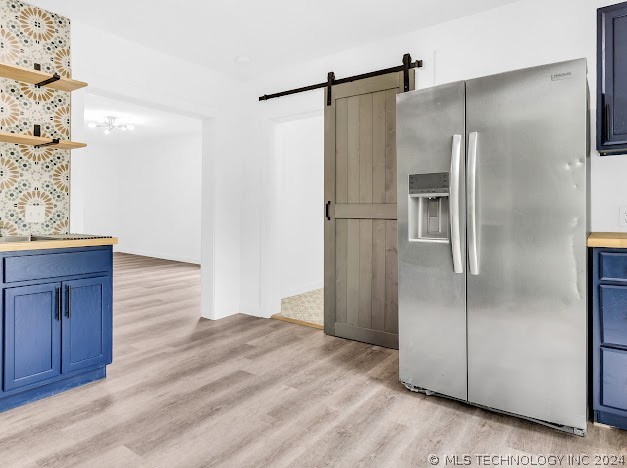 kitchen featuring stainless steel fridge with ice dispenser, light hardwood / wood-style flooring, a barn door, and blue cabinets