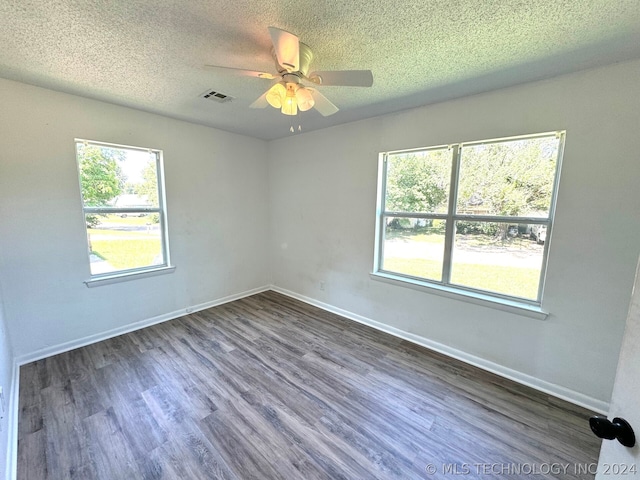 empty room with ceiling fan, a wealth of natural light, a textured ceiling, and hardwood / wood-style floors