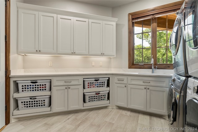 clothes washing area with sink, light hardwood / wood-style floors, cabinets, and stacked washer / drying machine