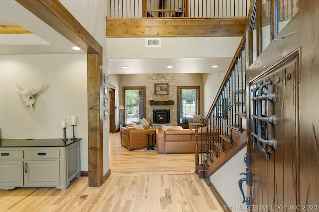 foyer entrance with a stone fireplace, light hardwood / wood-style floors, and a high ceiling