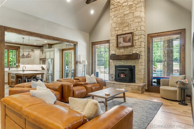 living room featuring light hardwood / wood-style flooring, high vaulted ceiling, and a stone fireplace