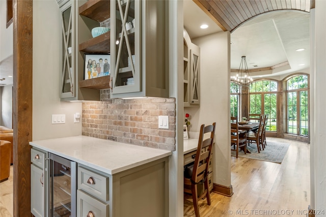 kitchen featuring beverage cooler, light wood-type flooring, a tray ceiling, decorative light fixtures, and a chandelier