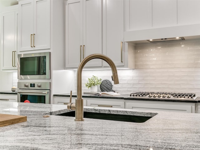 kitchen with light stone countertops, stainless steel appliances, backsplash, sink, and white cabinets