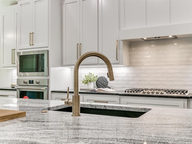 room details with white cabinetry, appliances with stainless steel finishes, light stone countertops, and sink