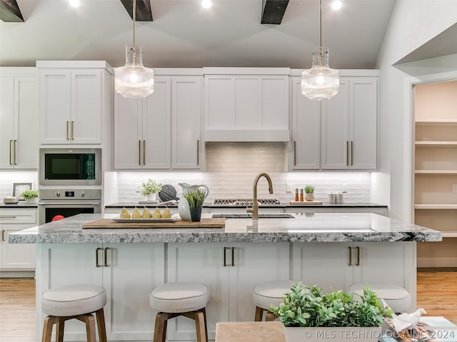 kitchen featuring light hardwood / wood-style floors, black microwave, a kitchen island with sink, oven, and tasteful backsplash