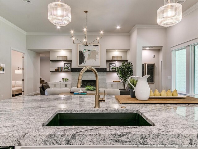 kitchen with sink, ornamental molding, light stone counters, and pendant lighting