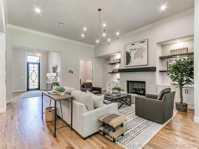 living room with built in shelves, crown molding, light wood-type flooring, and a brick fireplace