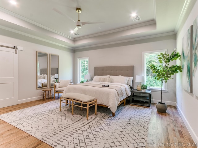 bedroom featuring ceiling fan, a barn door, a raised ceiling, ornamental molding, and hardwood / wood-style flooring