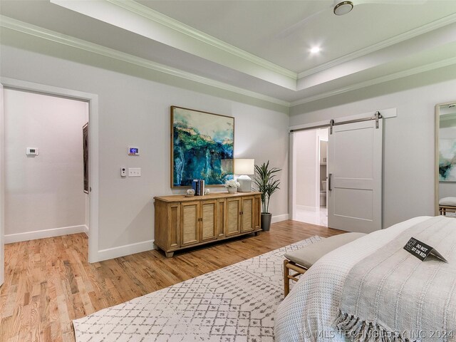 bedroom with a barn door, a tray ceiling, crown molding, and light wood-type flooring