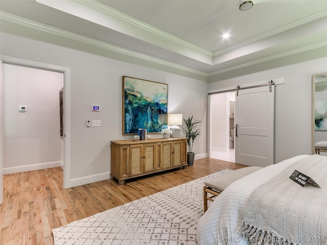 bedroom featuring a tray ceiling, ornamental molding, a barn door, and light wood-type flooring