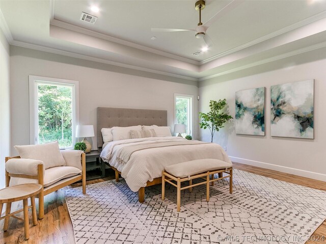 bedroom with hardwood / wood-style floors, ceiling fan, a raised ceiling, and crown molding