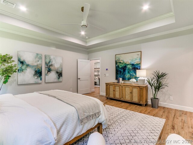 bedroom featuring wood-type flooring, ceiling fan, ornamental molding, and a tray ceiling