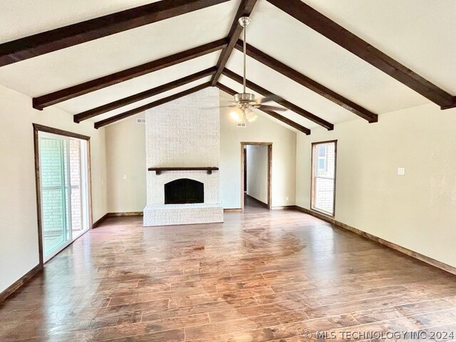 unfurnished living room featuring beam ceiling, hardwood / wood-style floors, brick wall, a fireplace, and ceiling fan