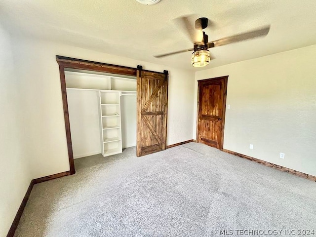 unfurnished bedroom with ceiling fan, light colored carpet, a barn door, a closet, and a textured ceiling