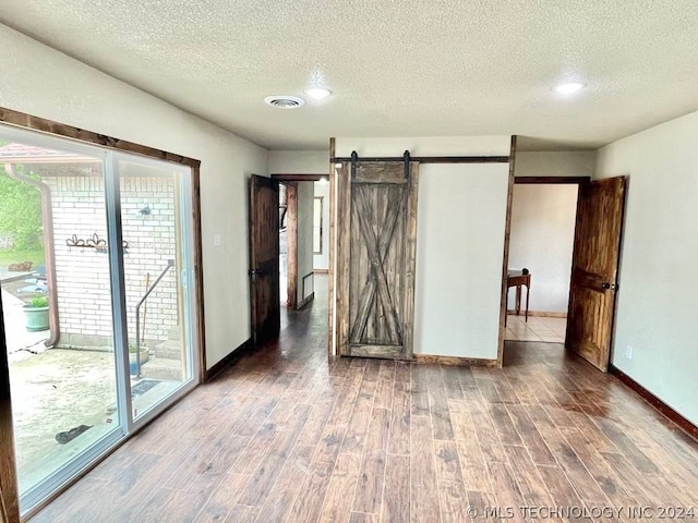 unfurnished bedroom featuring a textured ceiling, hardwood / wood-style floors, access to exterior, and a barn door