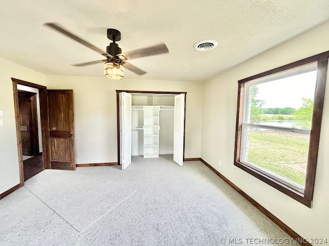 unfurnished bedroom featuring ceiling fan, light colored carpet, a closet, and a textured ceiling