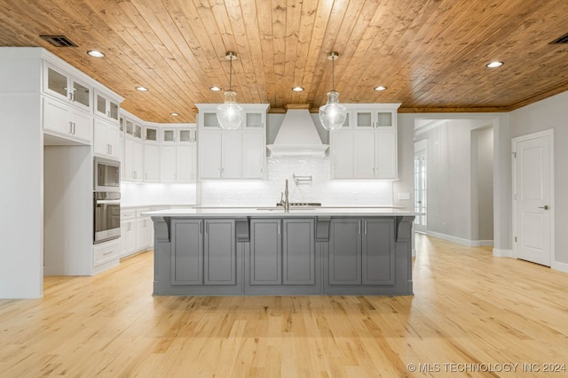 kitchen with wood ceiling, custom range hood, pendant lighting, a center island with sink, and white cabinetry