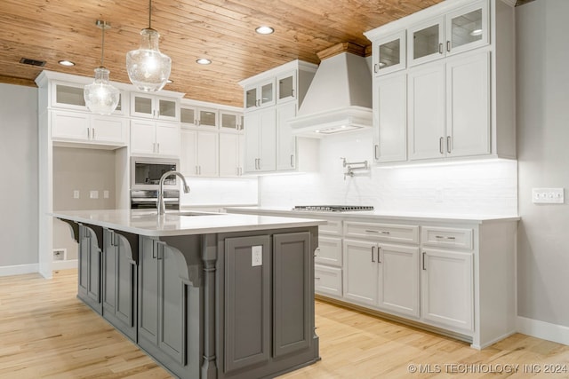 kitchen featuring premium range hood, white cabinetry, and an island with sink