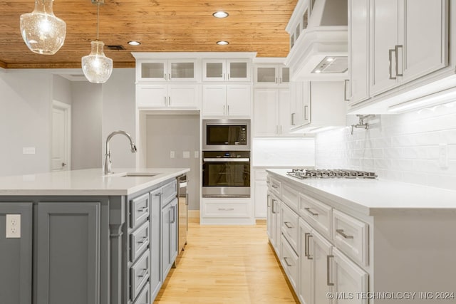 kitchen featuring custom exhaust hood, stainless steel appliances, a kitchen island with sink, sink, and pendant lighting