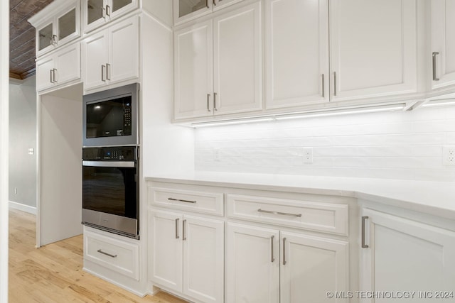 kitchen with white cabinets, appliances with stainless steel finishes, backsplash, and light hardwood / wood-style floors