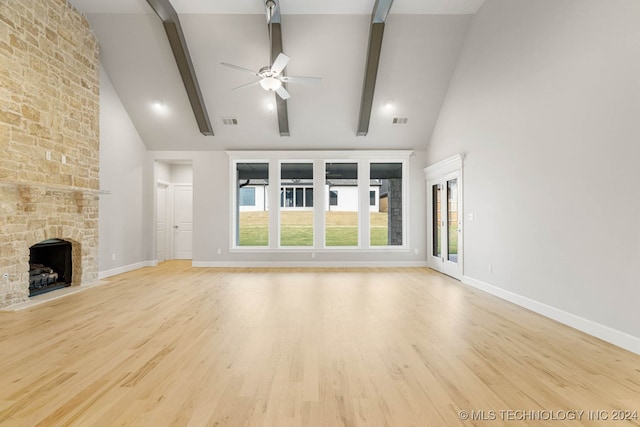 unfurnished living room featuring beam ceiling, light hardwood / wood-style floors, high vaulted ceiling, and a stone fireplace