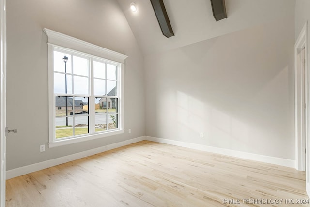 empty room featuring lofted ceiling with beams and light wood-type flooring