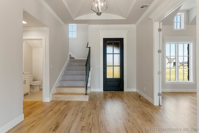 entrance foyer with lofted ceiling, ornamental molding, a notable chandelier, and light hardwood / wood-style flooring