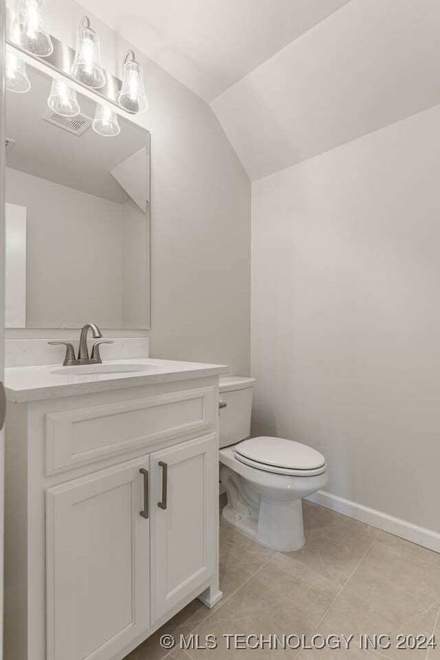 bathroom featuring tile patterned flooring, vaulted ceiling, toilet, and vanity