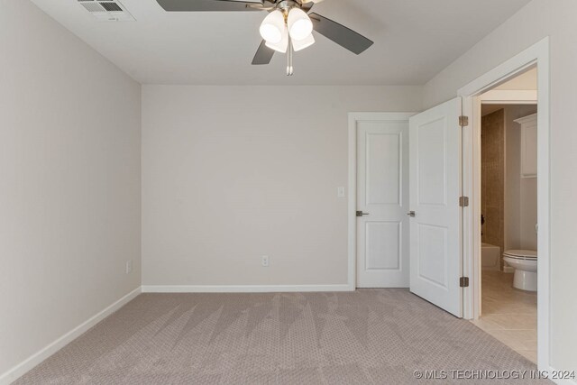 unfurnished bedroom with ceiling fan, ensuite bathroom, and light carpet