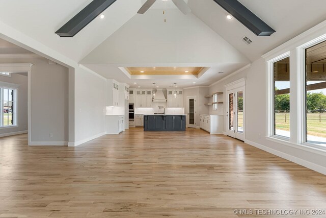 unfurnished living room with high vaulted ceiling, ceiling fan, a raised ceiling, and light hardwood / wood-style floors