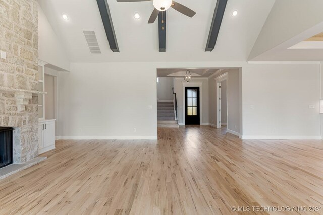 unfurnished living room featuring light wood-type flooring, high vaulted ceiling, ceiling fan, a stone fireplace, and beam ceiling