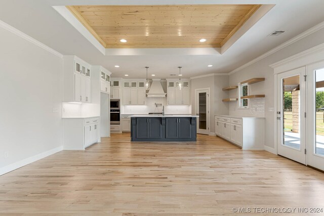 kitchen featuring an island with sink, custom exhaust hood, light wood-type flooring, and white cabinetry