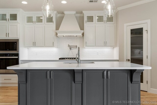 kitchen featuring a center island with sink, stainless steel oven, premium range hood, and white cabinetry