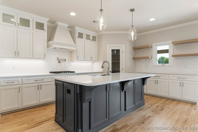 kitchen featuring white cabinetry, a center island with sink, custom range hood, and sink