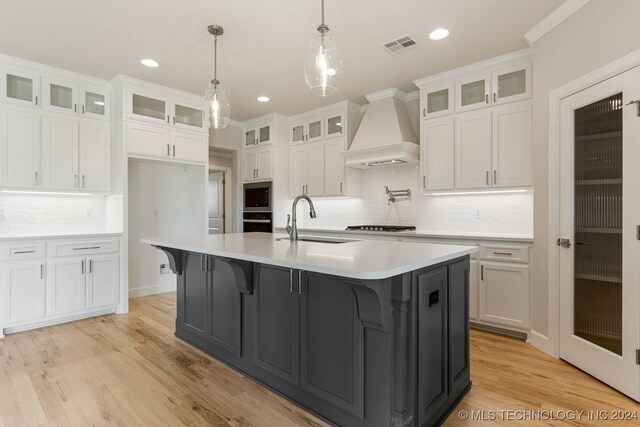 kitchen with white cabinets, premium range hood, a kitchen island with sink, and sink