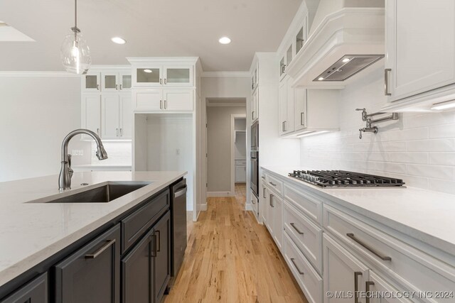 kitchen with white cabinets, decorative light fixtures, light wood-type flooring, custom exhaust hood, and sink