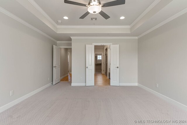 unfurnished bedroom featuring ornamental molding, a raised ceiling, ceiling fan, and light colored carpet