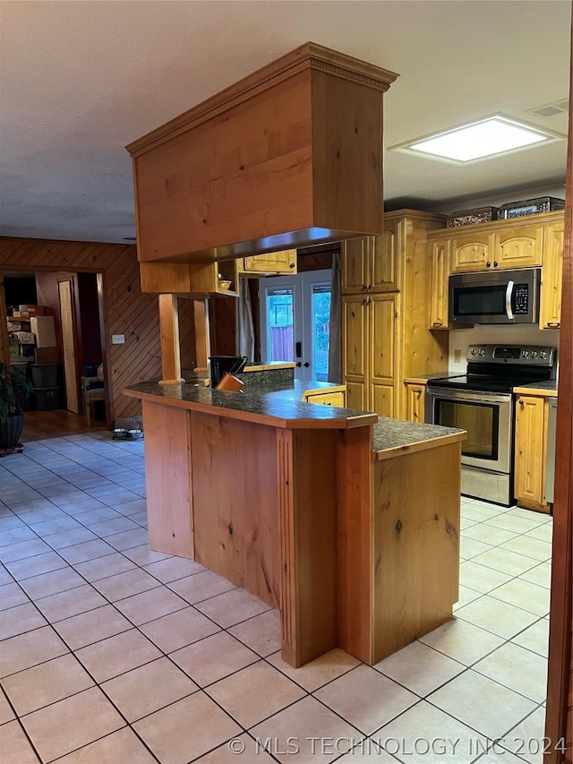 kitchen featuring light tile patterned flooring, appliances with stainless steel finishes, kitchen peninsula, and wood walls