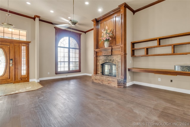 unfurnished living room featuring ceiling fan, a brick fireplace, crown molding, and dark wood-type flooring