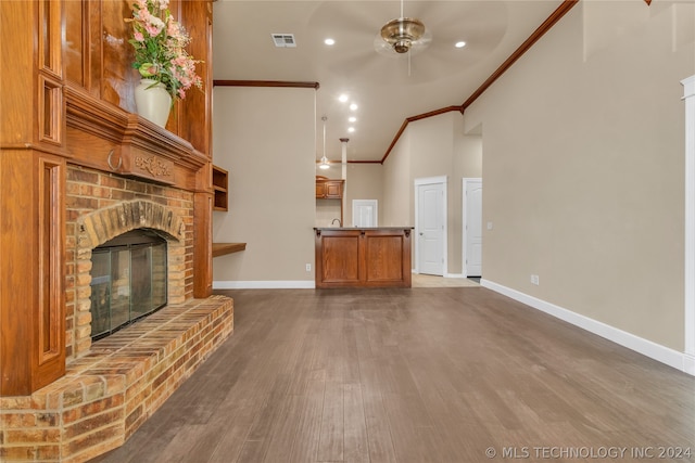 unfurnished living room featuring crown molding, dark wood-type flooring, a brick fireplace, vaulted ceiling, and ceiling fan